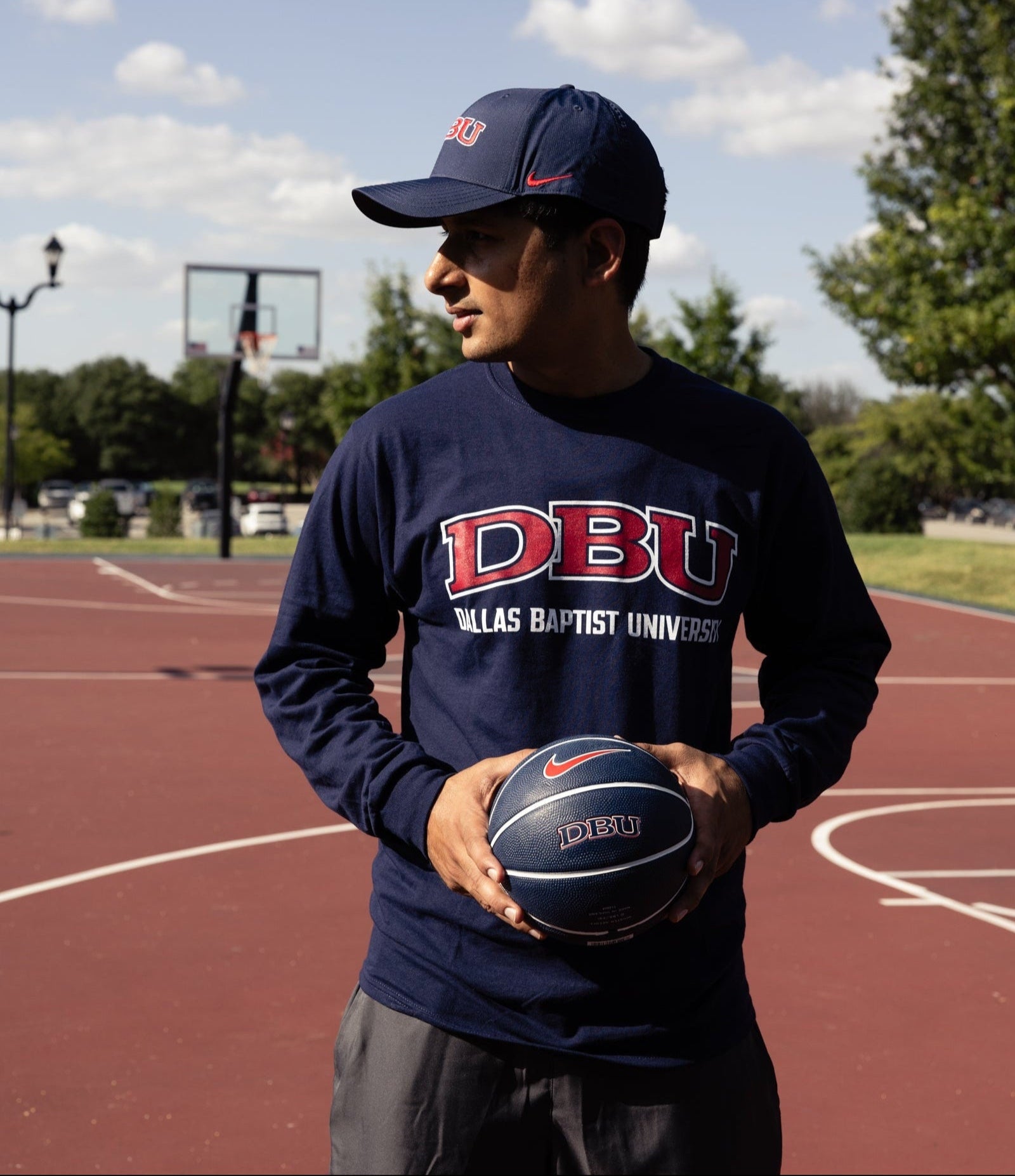 Person wearing a navy long-sleeve shirt and cap with 'DBU' holding a basketball on a court.