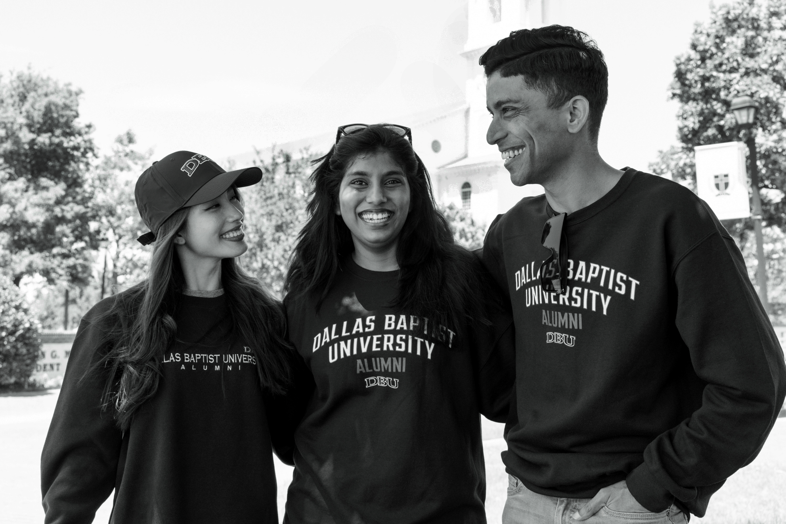 Three individuals wearing Dallas Baptist University alumni sweatshirts outdoors.