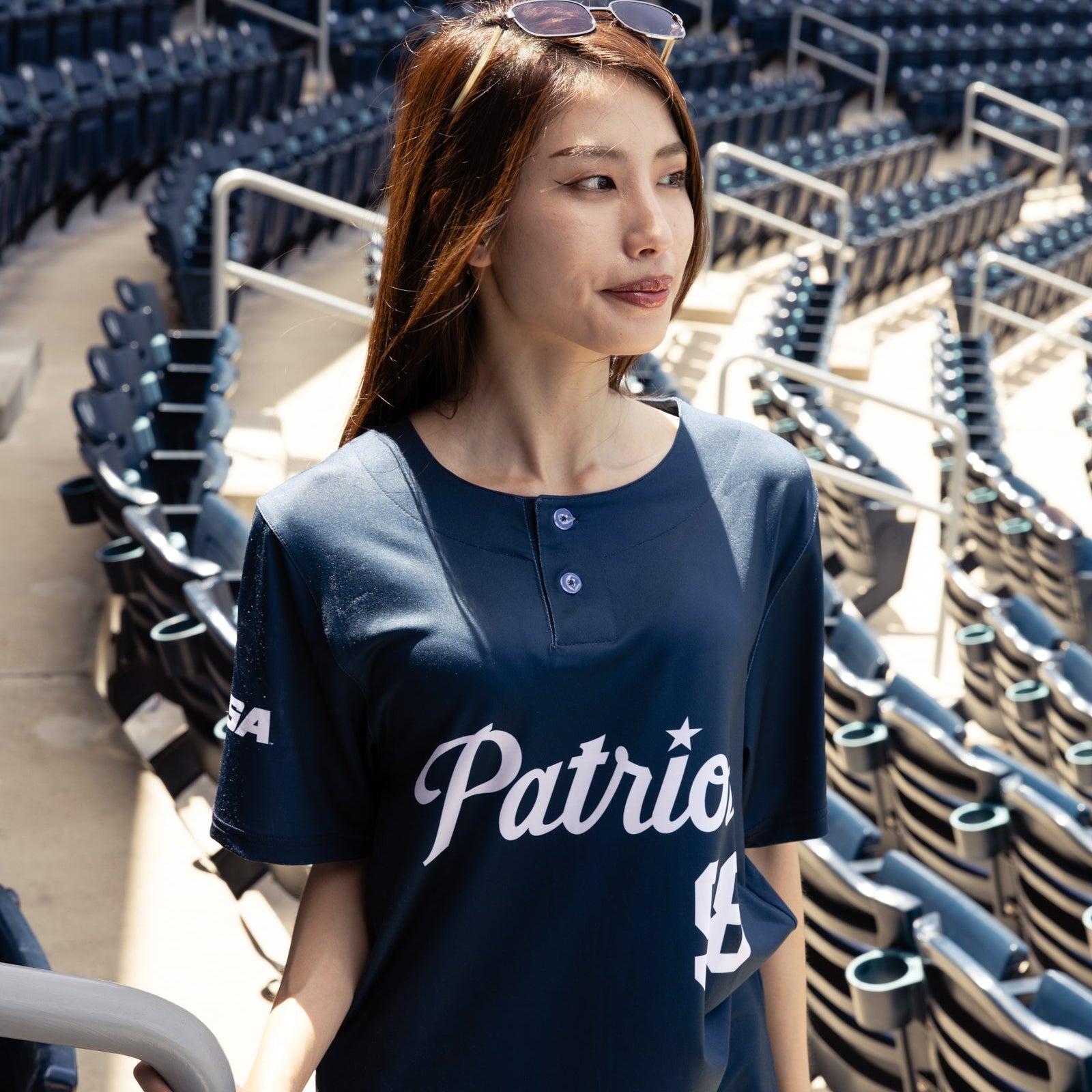 Woman wearing a navy blue 'Patriots' shirt in an empty stadium.