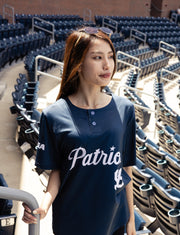 Woman wearing a navy blue 'Patriots' shirt in an empty stadium.