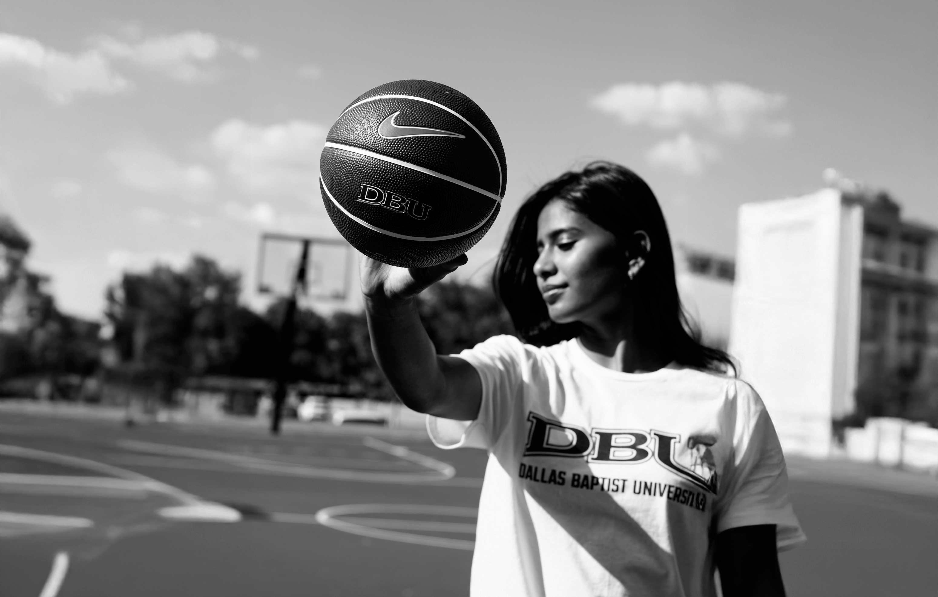 Person holding a basketball on an outdoor court with 'DBU' branding